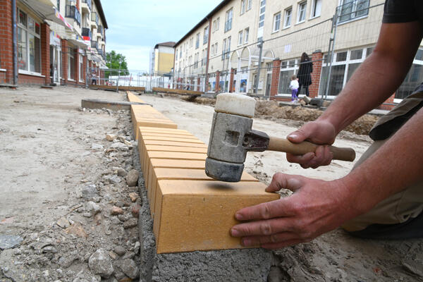 Bild vergrößern: Holzhammer schlägt auf gelben Klinker: Das Veltener Band wird auf dem Marktplatz gesetzt.