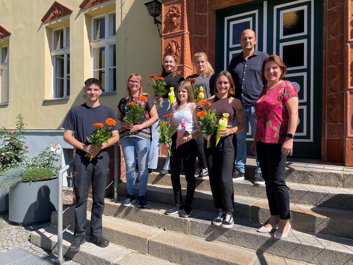 Bild vergrößern: Die Bürgermeisterin Ines Hübner und der Personalchef Heiko Rüchel-Machler stehen mit den Auszubildenen auf der Treppe vor dem Rathaus. Sie halten Blumen in der Hand.