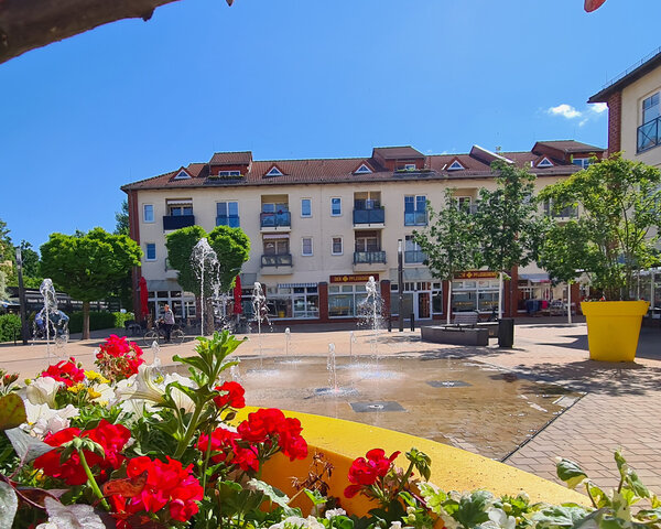 Bild vergr&ouml;&szlig;ern: Das Wasserspiel mit Wasserfont&auml;nen bietet eine Erfrischung an hei&szlig;en Tagen. Im Vordergrund sind rote Blumen.