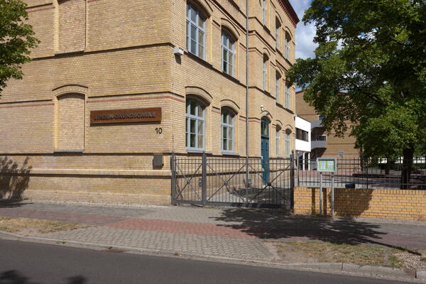 Bild vergrößern: Das Eingangstor mit dem verklinkerten Schulgebäude.